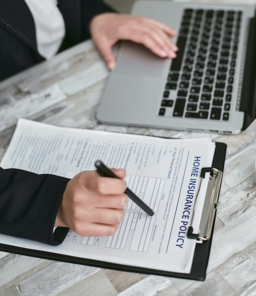 pexels-photo-7734611-7734611 An adult reviews and signs a home insurance policy document on a clipboard next to a laptop.